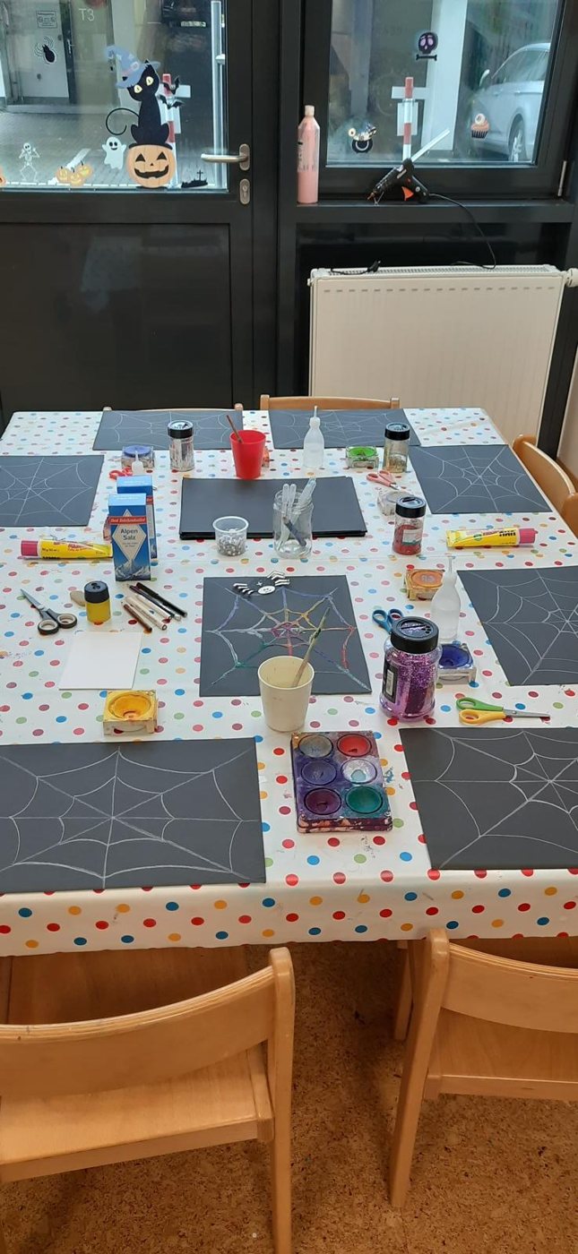 Gedeckter Basteltisch mit Spinnennetzen, Farben und Glitzer